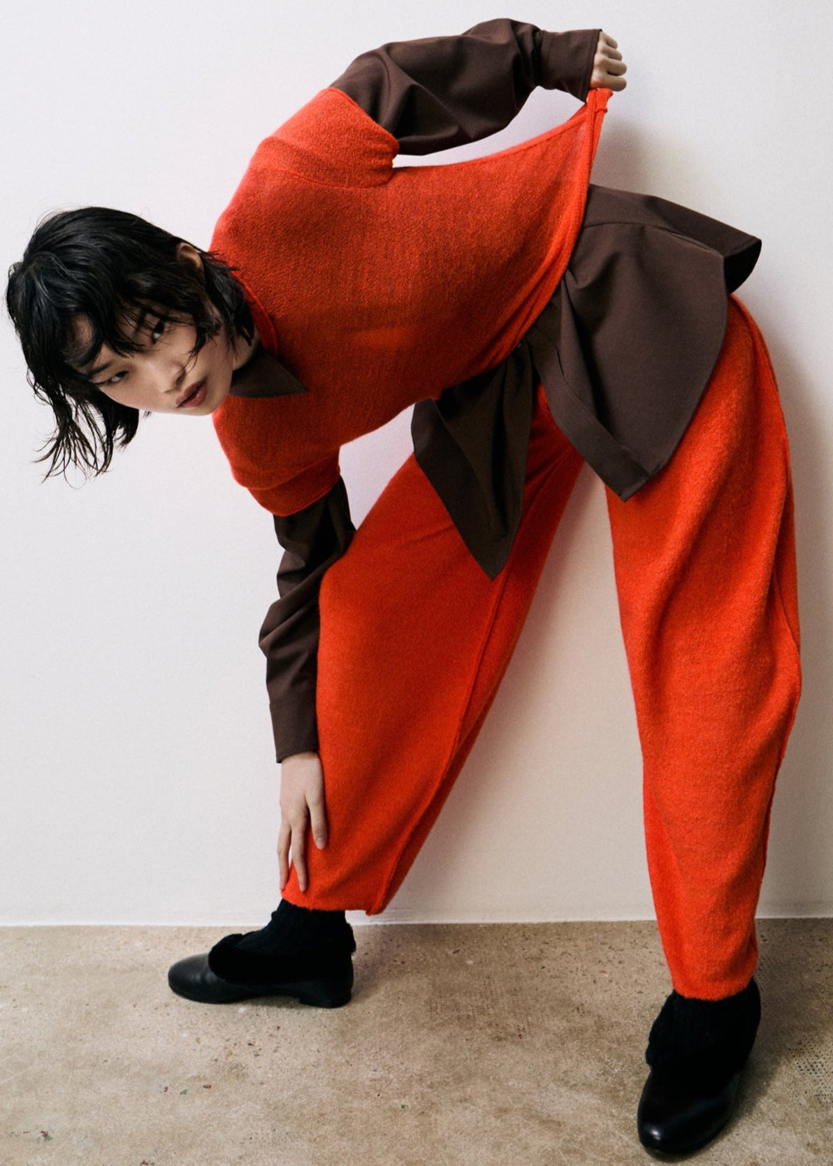 Person wearing a red and brown outfit posing against a white wall.