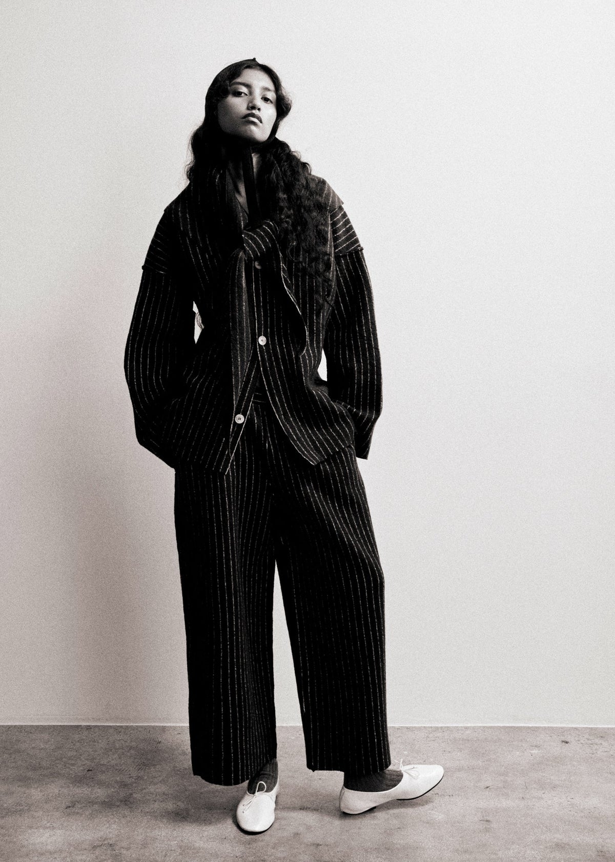 Person wearing a black pinstripe suit with a scarf against a plain background