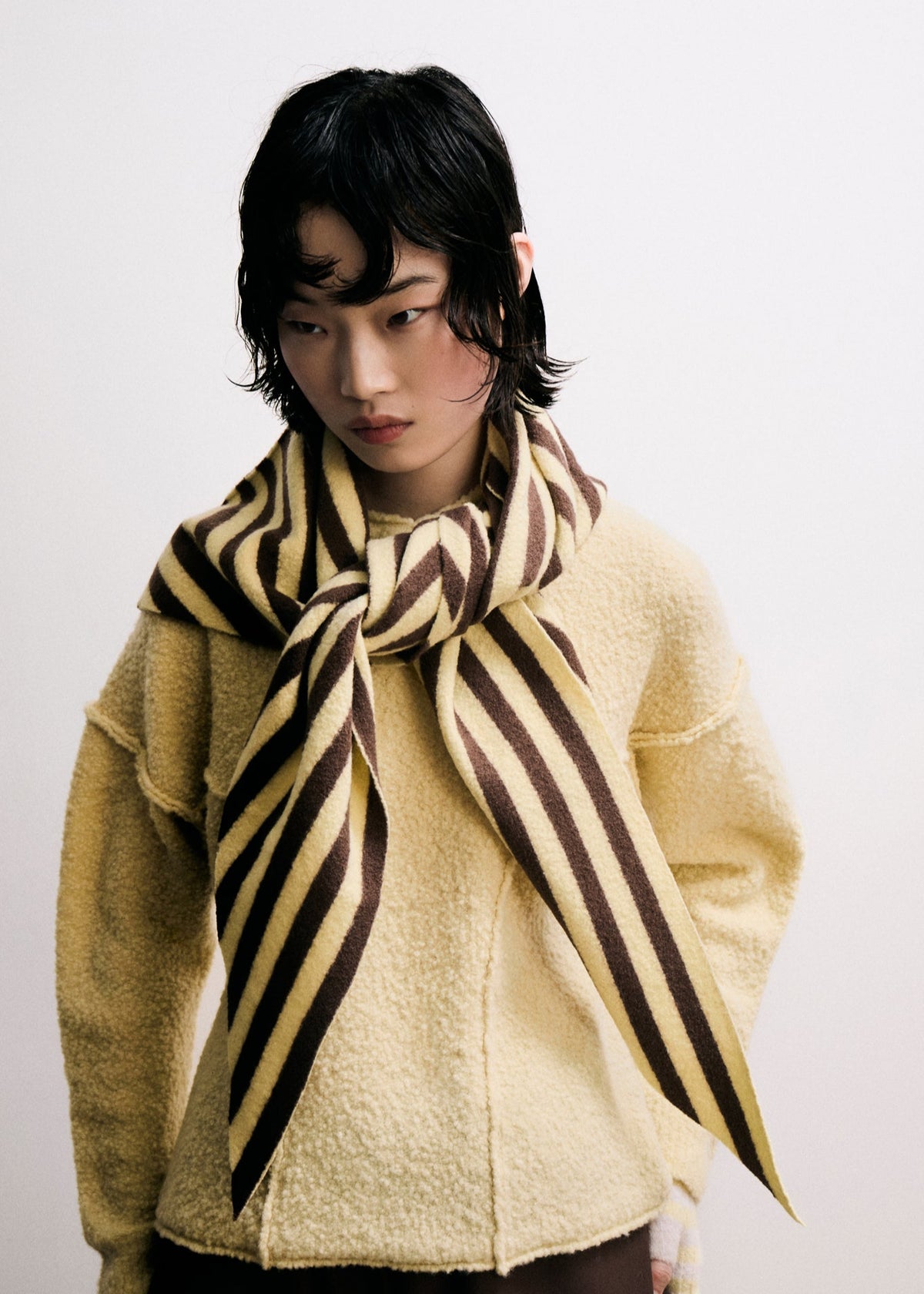 Person wearing a yellow sweater and striped scarf against a white background