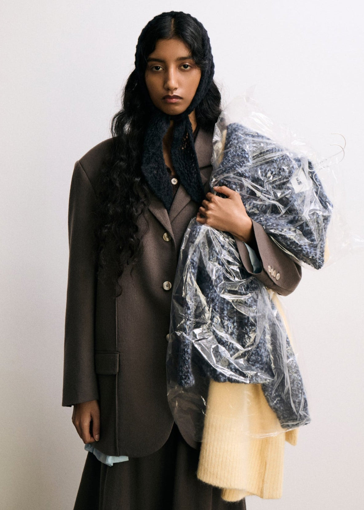 Woman in a suit holding a transparent raincoat against a white background