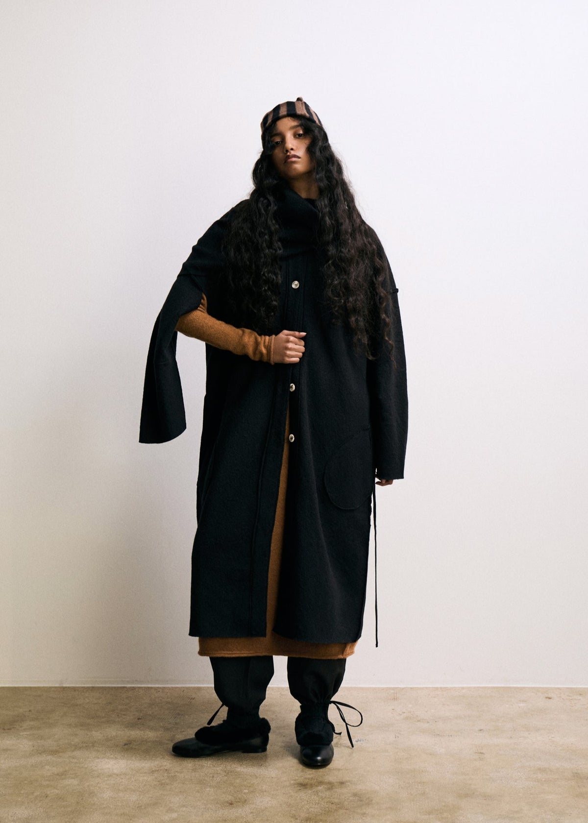 Person wearing a long black coat with a hat against a white background