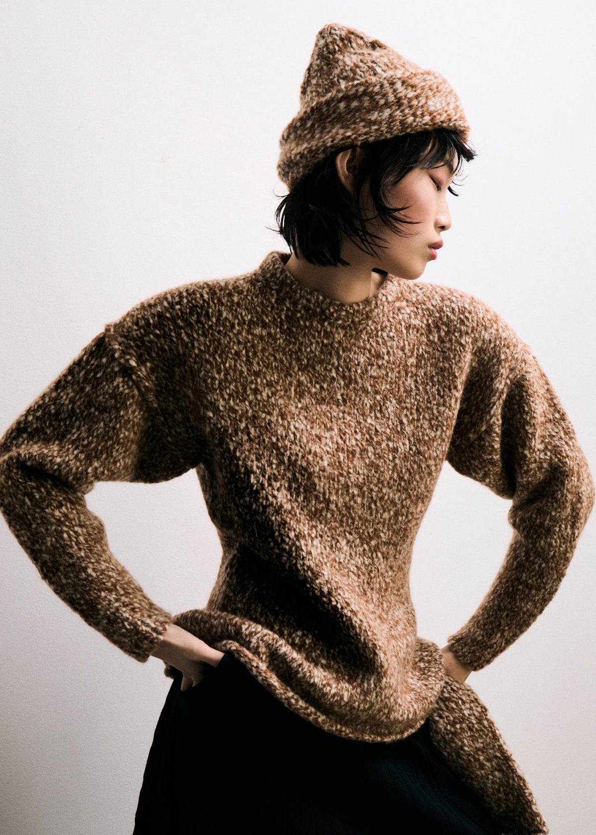 Person wearing a brown textured sweater and hat against a plain background