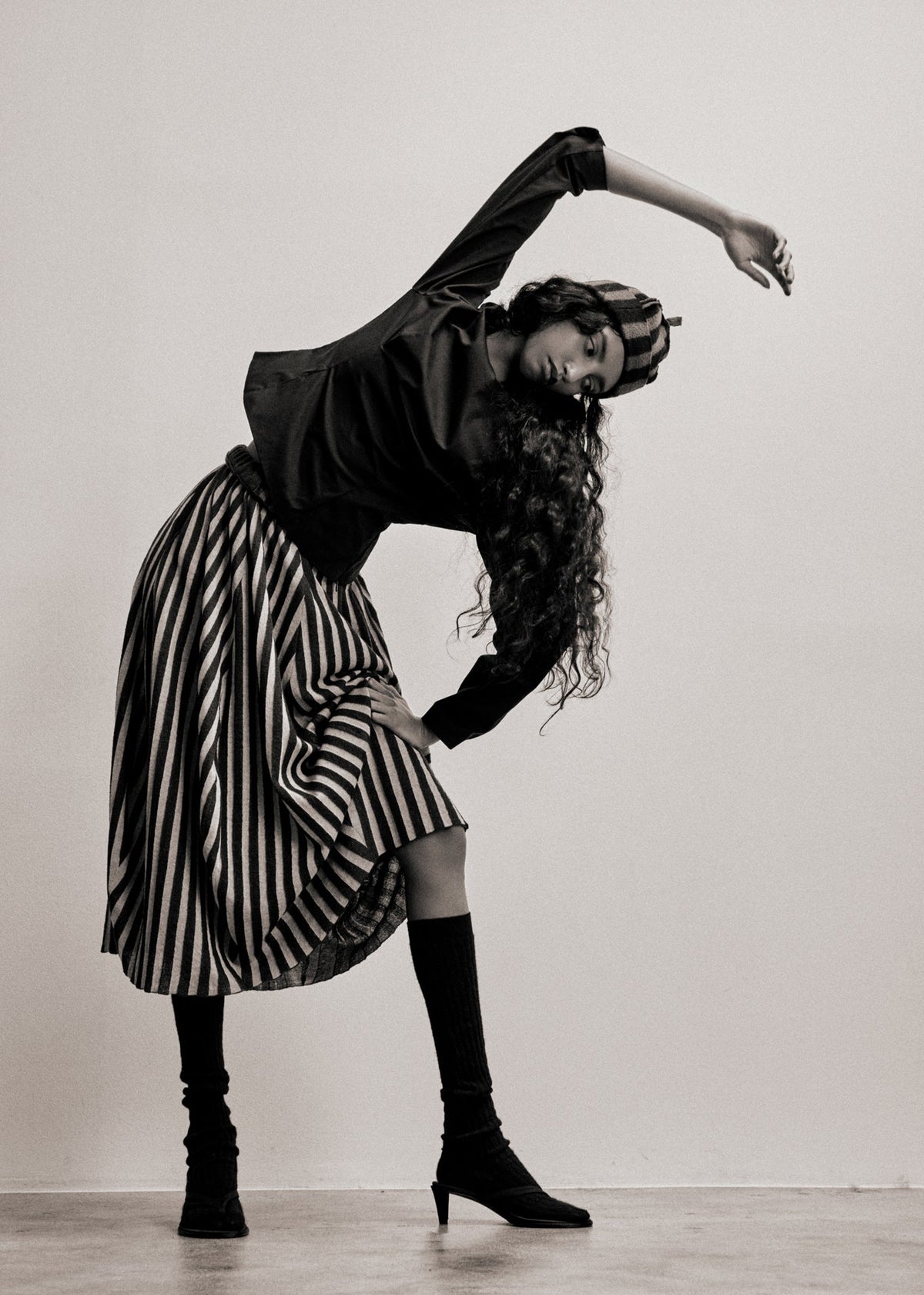 Person in a black and white striped skirt with long hair, posing against a plain background