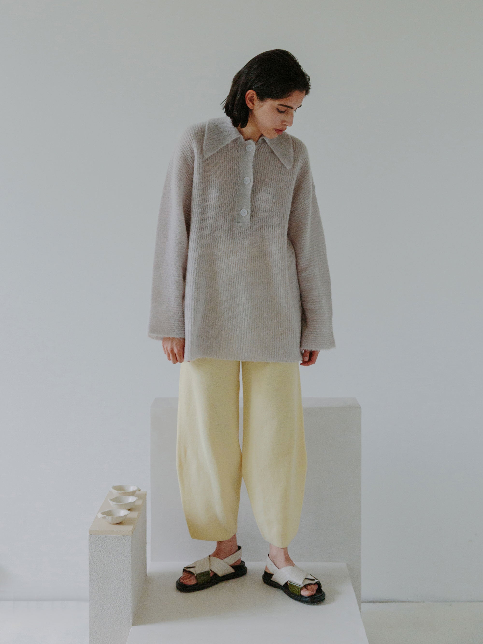 Esra wearing the FUKU polo sweater and NAIFU pants with chair N04F002 and ceramics. Photographed by Marina Denisova.